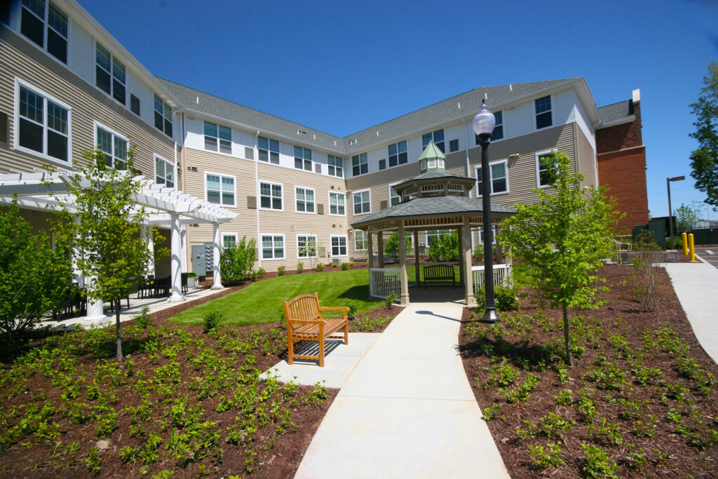 Senior Living at Cambridge building exterior with a bench and gazebo along a walking path.