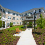 Senior Living at Cambridge building exterior with a bench and gazebo along a walking path.